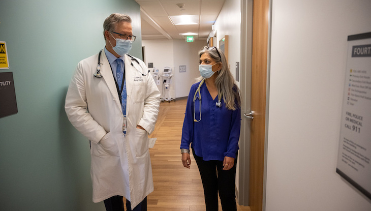 Two physicians are seen talking together in a medical clinic.